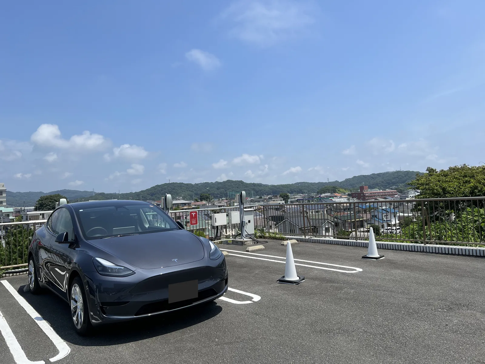 屋上のテスラ充電区画に停めたグレーのテスラ・モデルYと奥に並ぶウォールコネクター